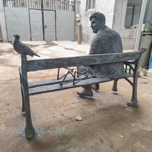 bronze statue man sitting on park bench with a bird